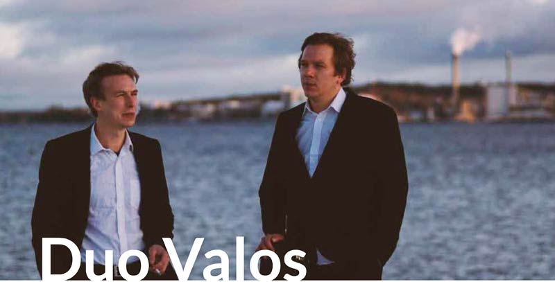 Foto der beiden Musiker vor einer Meeresbucht mit Stadtsilhouette im Hintergrund