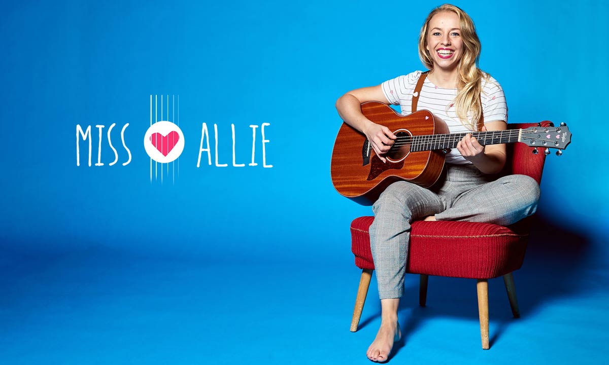 Miss Allie auf einem roten Sessel mit Gitarre