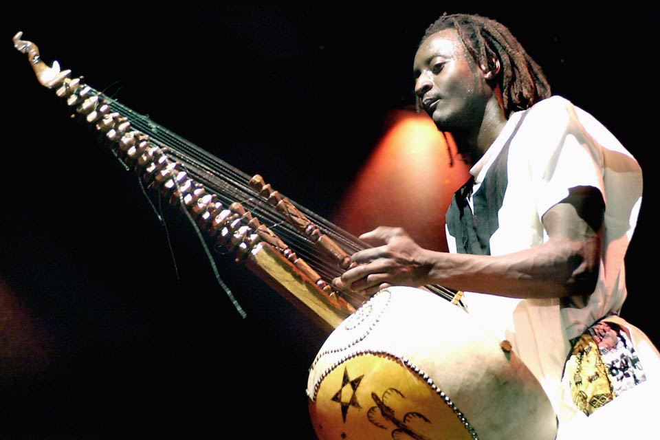 Kekso L. Diabang mit afrikanischer Kleidung und Frisur spielt auf einer Kora, ein Saiteninstrument mit langem Hals und einem großen, kürbisförmigen Körper